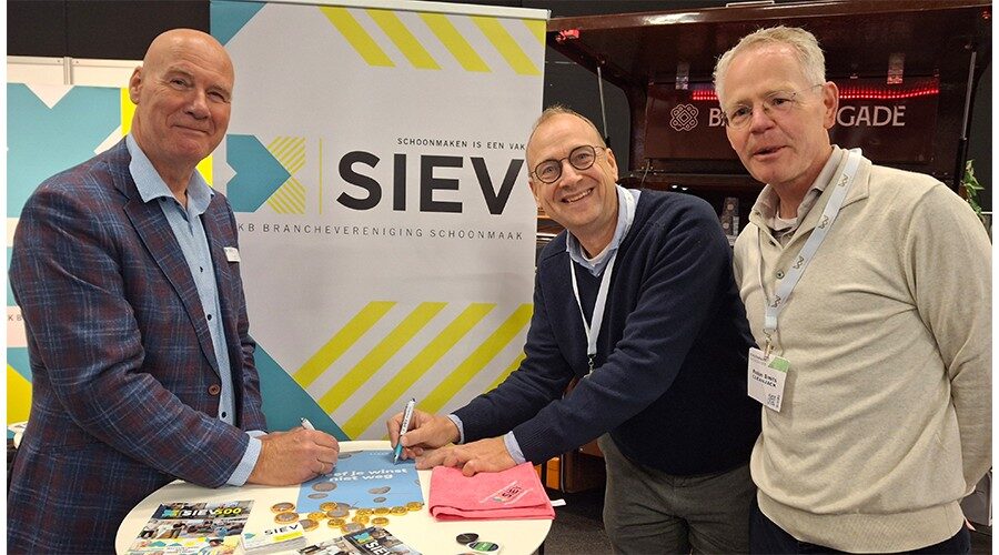 Robin Smits kijkt hoe zijn collega Niels van den Berg  met SIEV-voorzitter Paul Fok de samenwerkingsovereenkomst ondertekent.